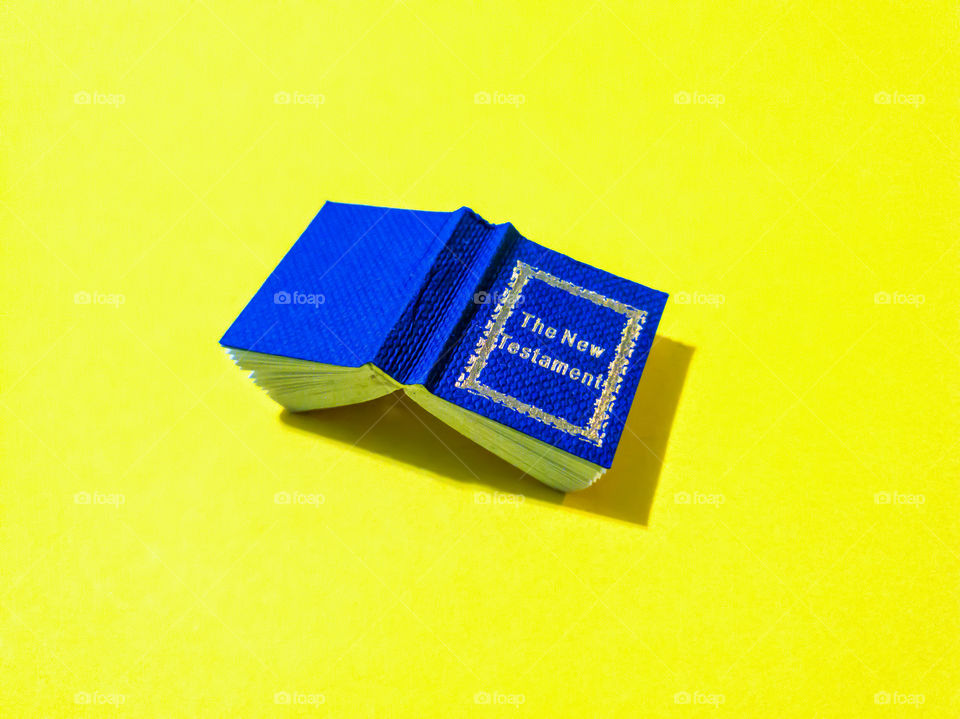 Flat lay of a royal blue tiny minirature  New testament Bible on a yellow background.