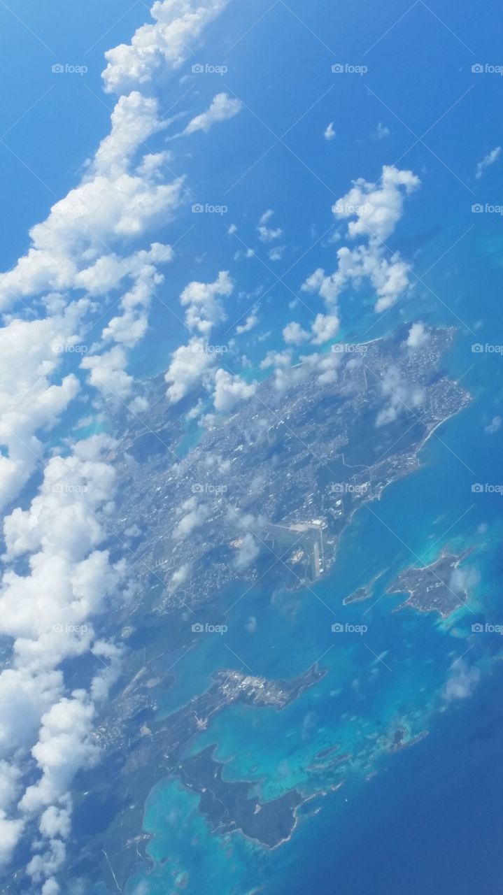 Birdseye view flying over the Caribbean. Clouds relaxing above the people, land and ocean below.
