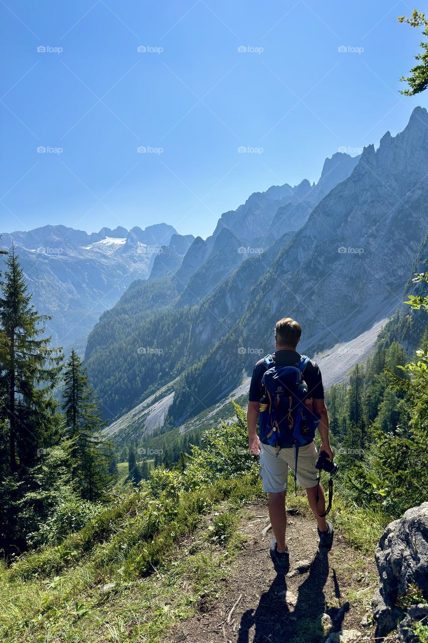 Hiker watches the stunning view of the mountains on a sunny day, shot from behind 