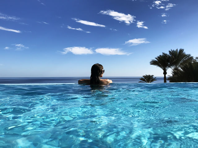 Young woman enjoying her tropical vacation at the swimming pool and amazing view above the sea 