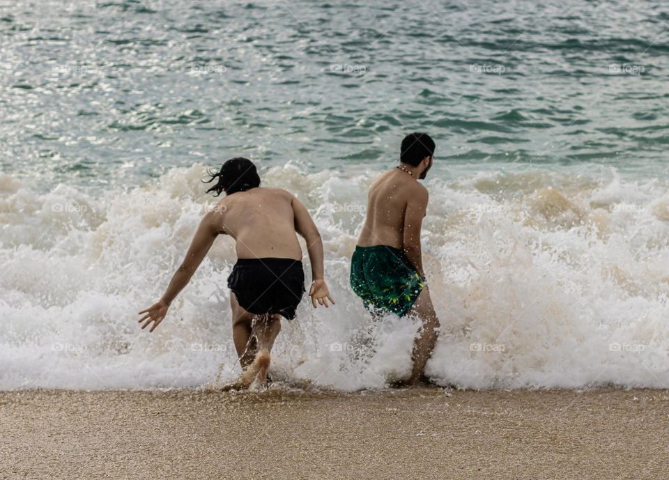 2 young man race into the crashing Atlantic waves at Praia da Nazaré, Portugal 