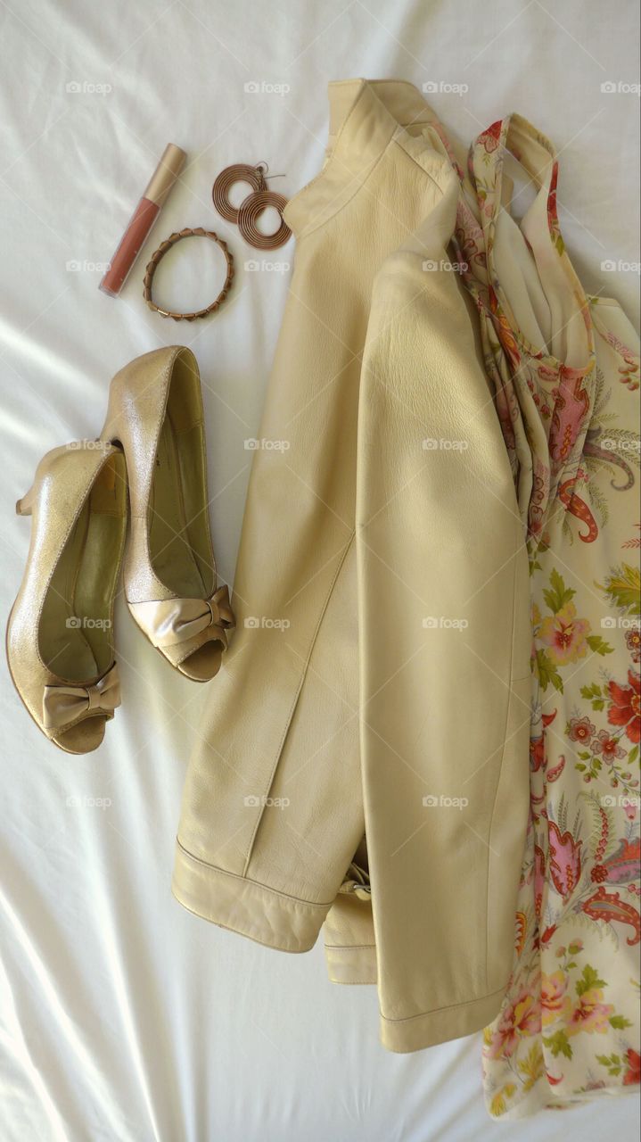 flat lay with beige leather jacket with floral dress, gold pumps, and copper accessories
