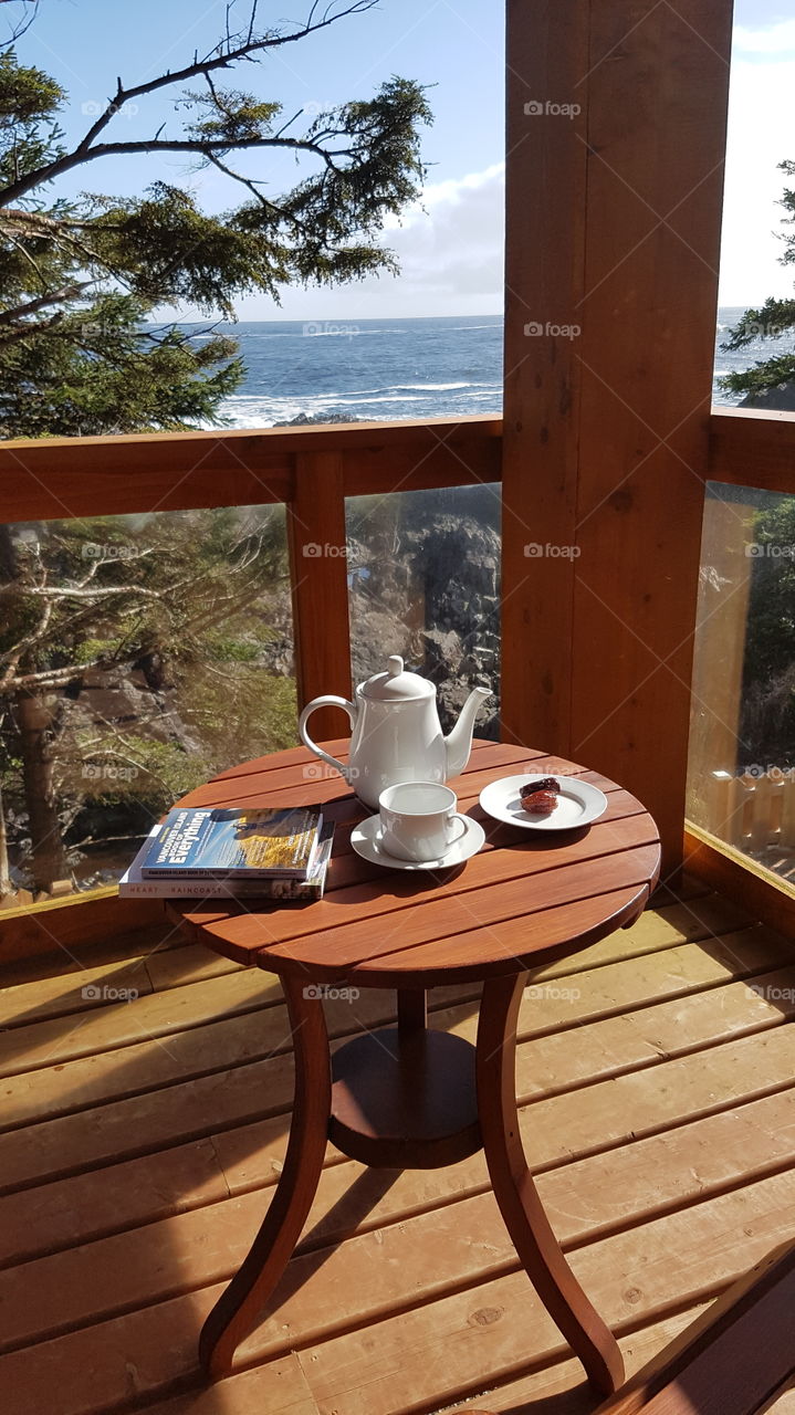 holiday relaxation on wooden deck of holiday home with ocean views over a rocky shore,  tea and a good travel book