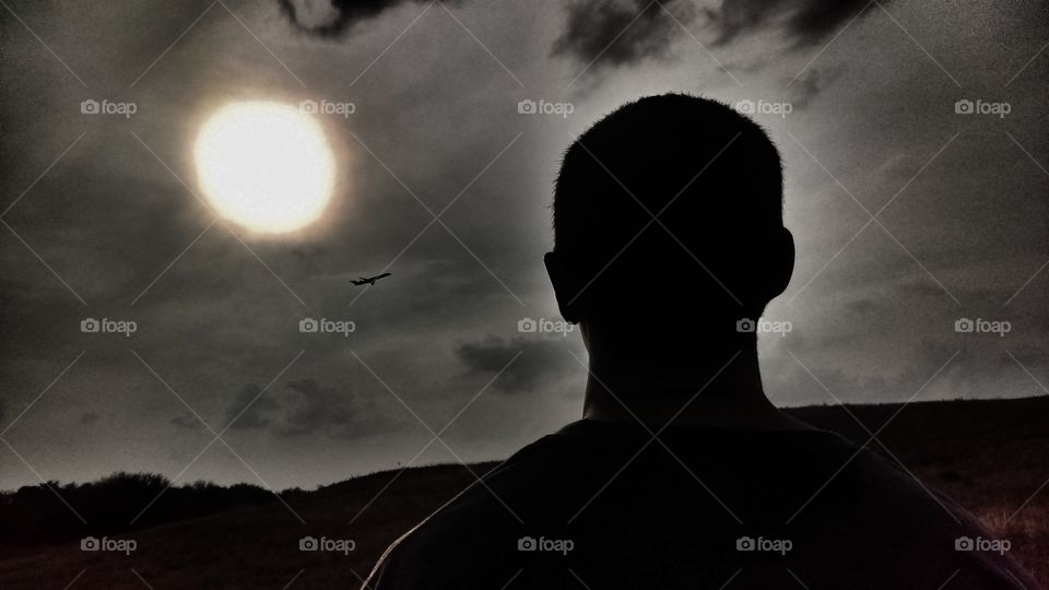 Silhouette of a man viewing a plane fly just below the sunset