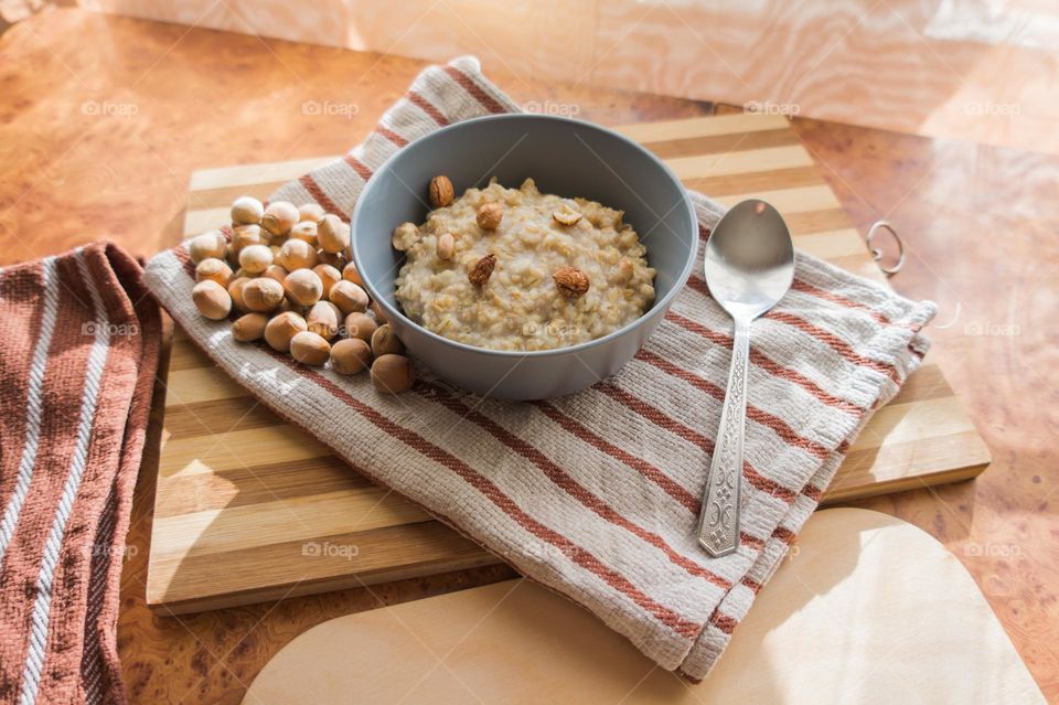 Cooked oatmeal in a deep gray plate with hazelnuts and honey.
