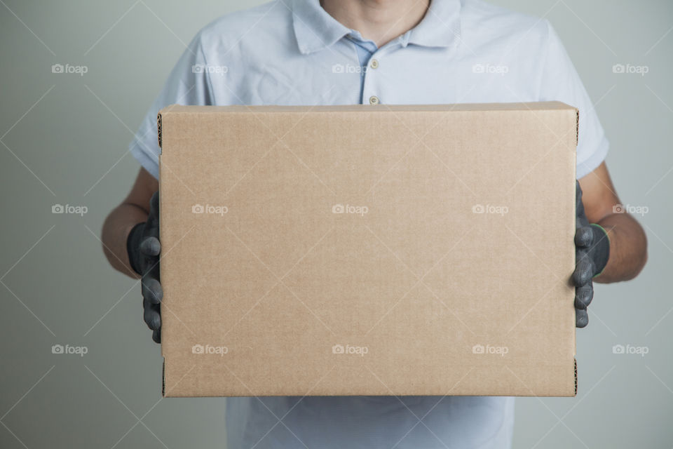 Detail of man with black gloves holding a cardboard box for delivering products on gray background. Delivery concept. Delivery service concept. Copy space.