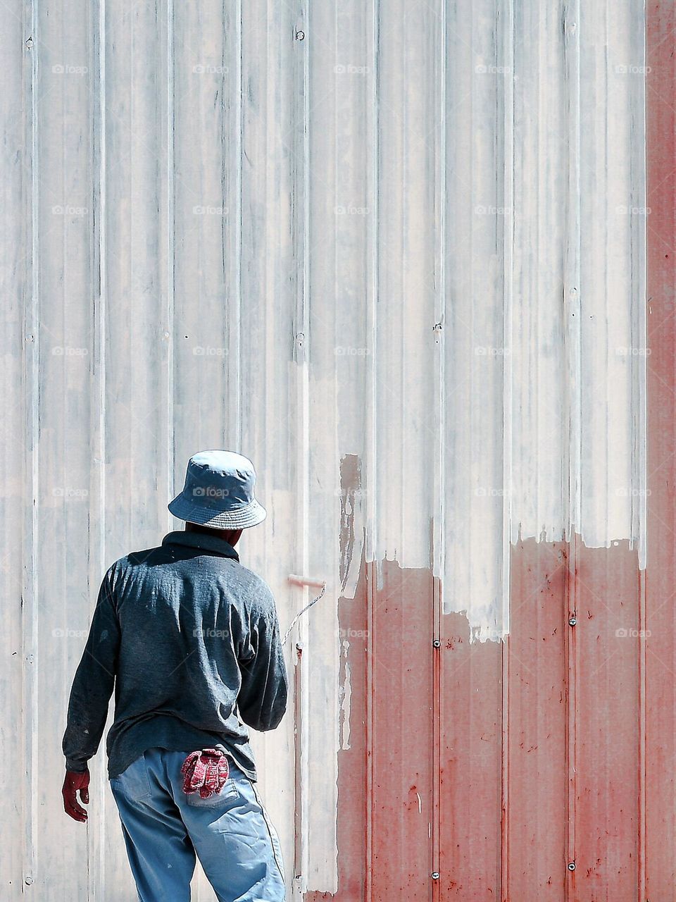 A painter working on a metal fence at a construction site in bright sunny day