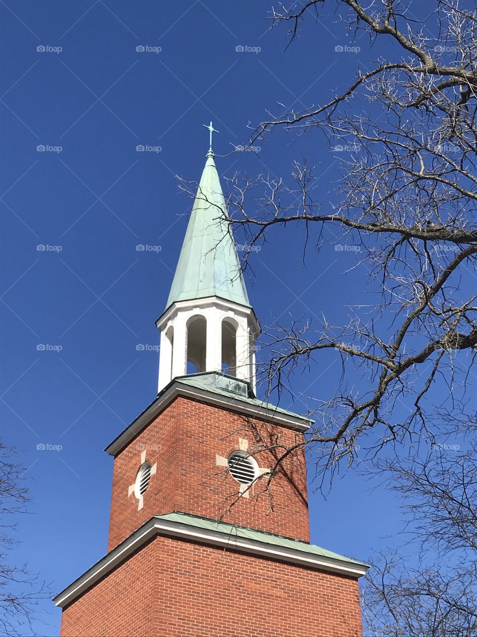 Church steeple bell tower & cross with blue sky and branches  