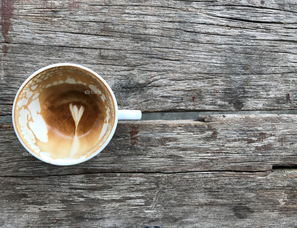 top view of white cup of finished latte coffee with white flower shape latte art left in a cup on natural wooden table with copy space on right side of frame