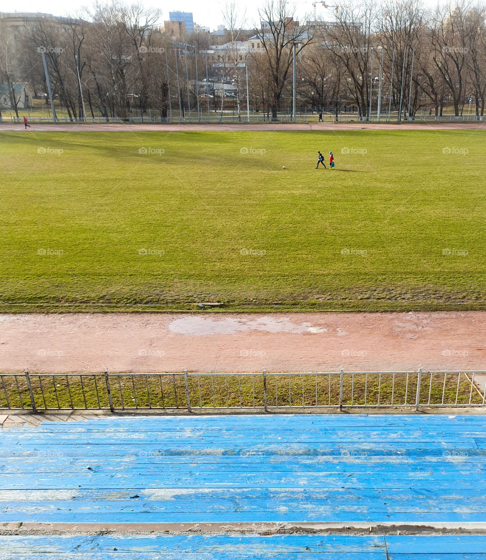 The beginning of spring, a boy with a girl on the football field playing ball. View from the podium on an open football field with young grass and children playing ball