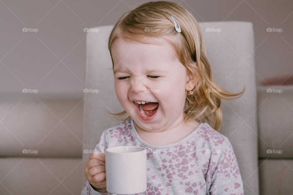 Toddler girl drinking tea, laughing. Family moment at home. 