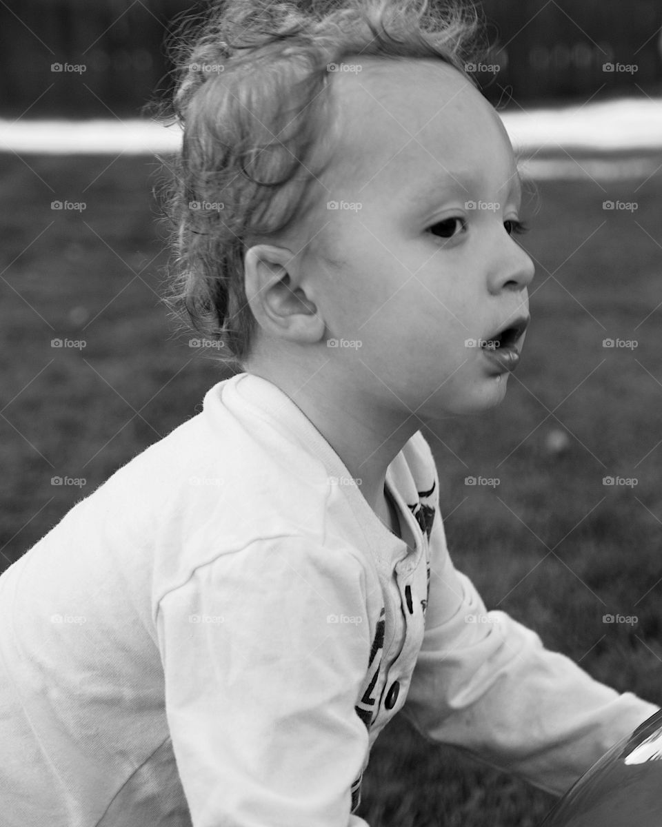 A small toddler boy strains to control a giant rubber ball on a sunny summer day. 