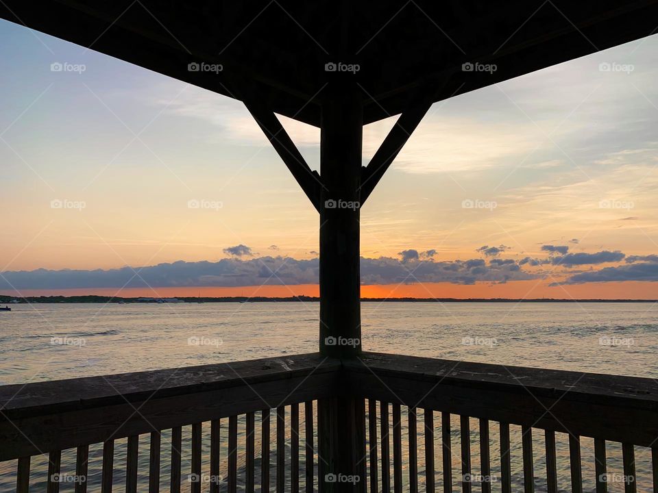 Sunset In The Horizon With Deep Orange Color Sighting From Gazebo On The Dock By The Island Reflecting On The Water.