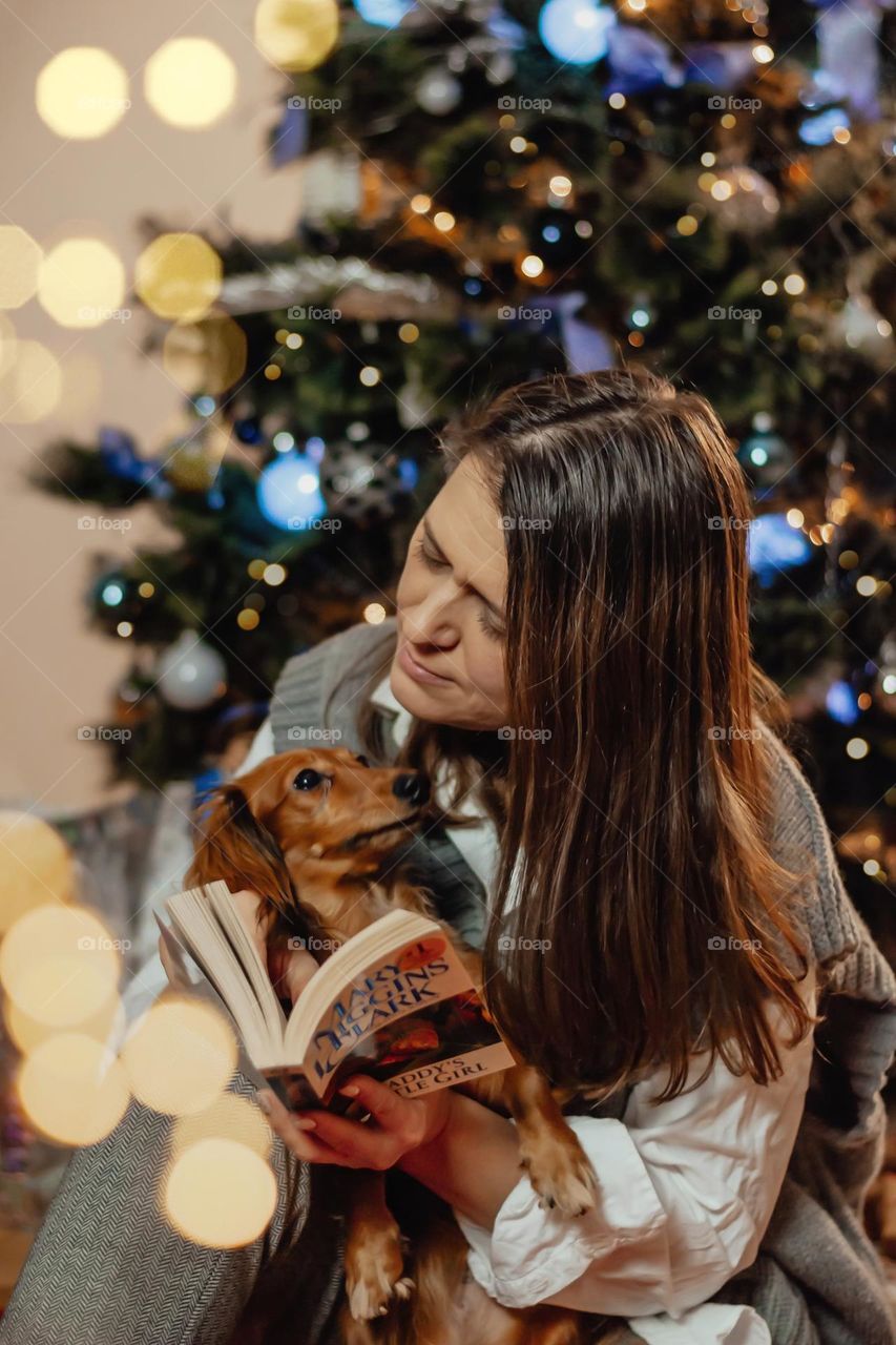 Beautiful woman with pet dog dashboard at home, reading book, eve Christmas and new year’s 