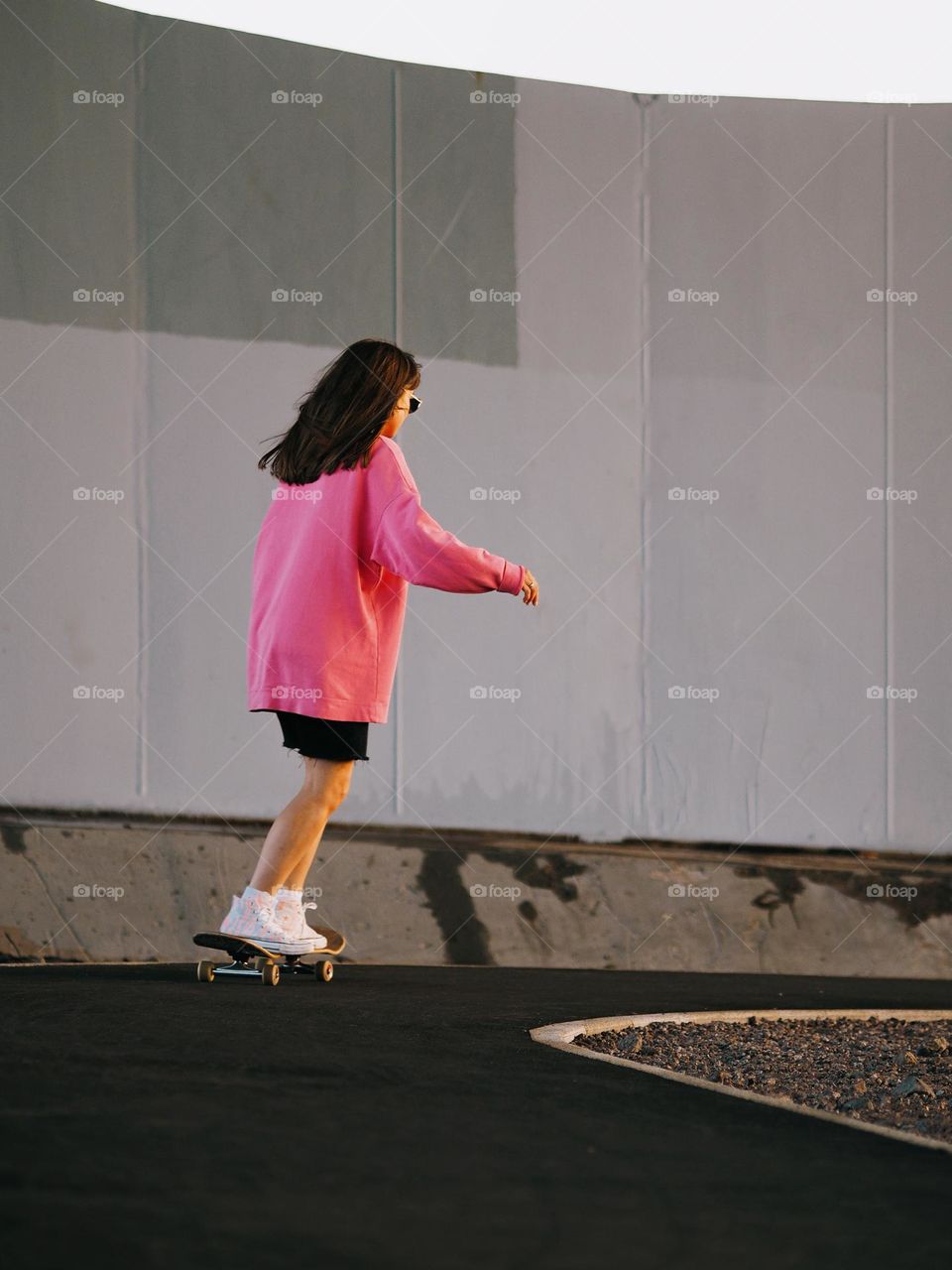 Young brunette girl in a pink sweatshirt skateboarding on a warm summer day