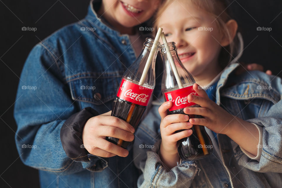 stylish children, dressed in denim clothes, drinking Coca-Cola.  They eat, relax, communicate at home.  sister and brother drink coca cola