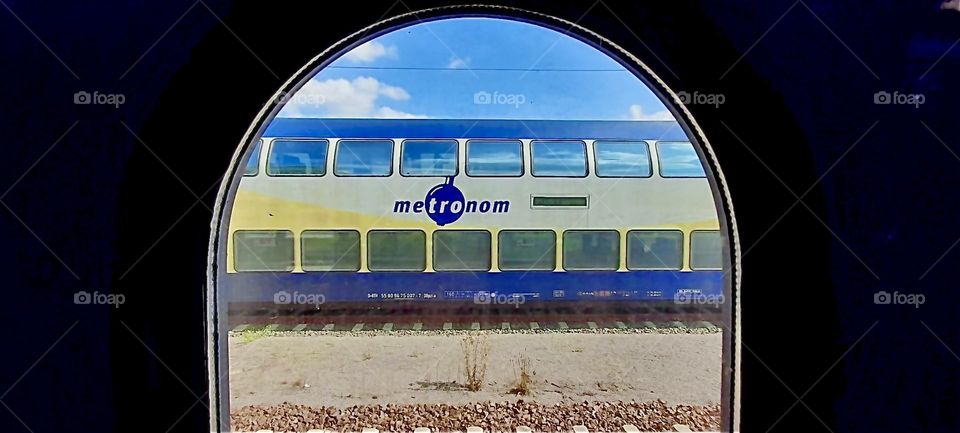 Seen through one of the large arched opening a train in the stunning complimentary colors of bright indigo and yellow can be seen. 2022. Hypnotic Productions