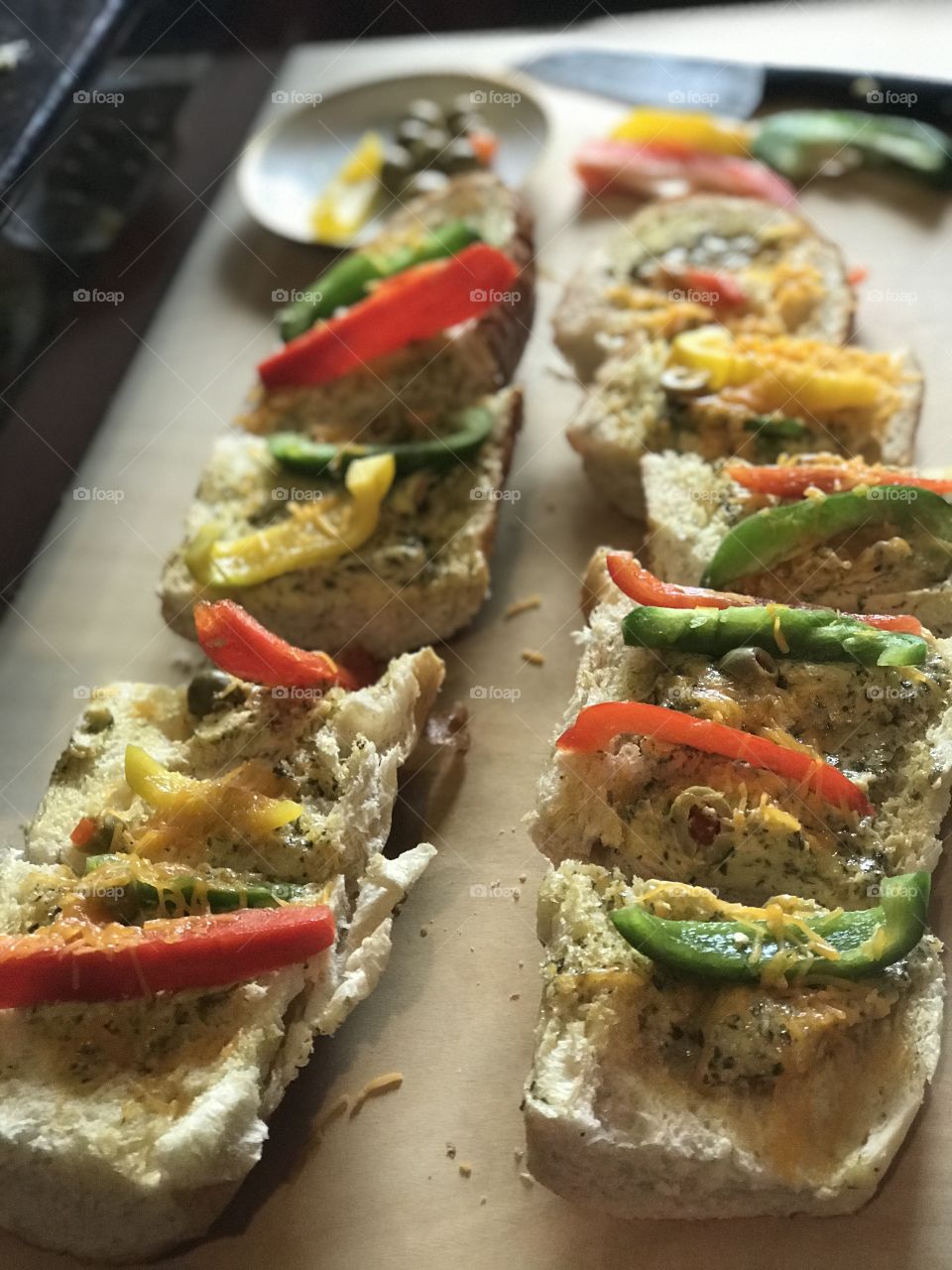 A garlic bread bell pepper Sandwich with green Olives and cheese being prepared on the wooden cutting board. 