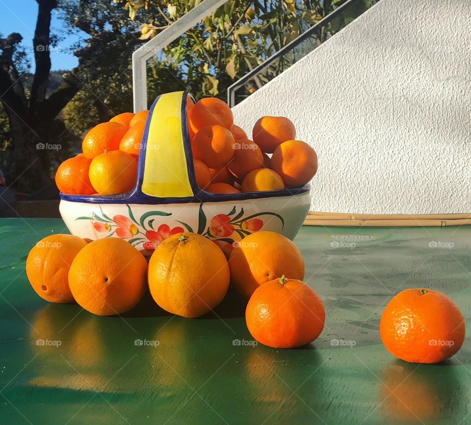 A ceramic fruit basket full of oranges outside on a green table