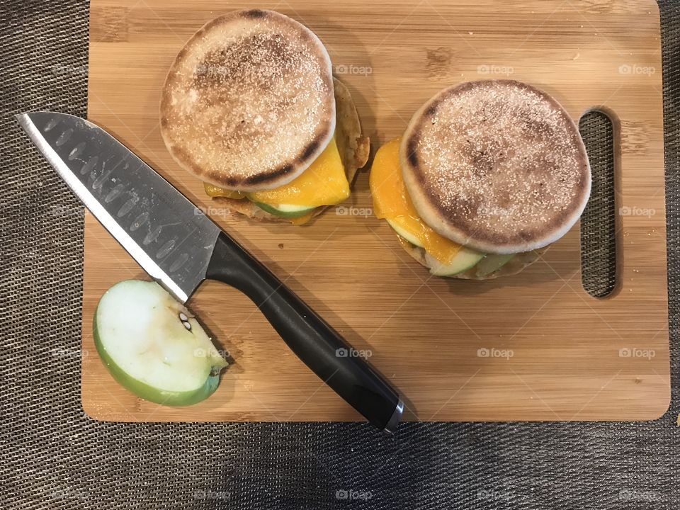 An apple and cheese melt sandwich on English muffin bread on a cutting board with an apple slice and a knife for cutting. USA, America