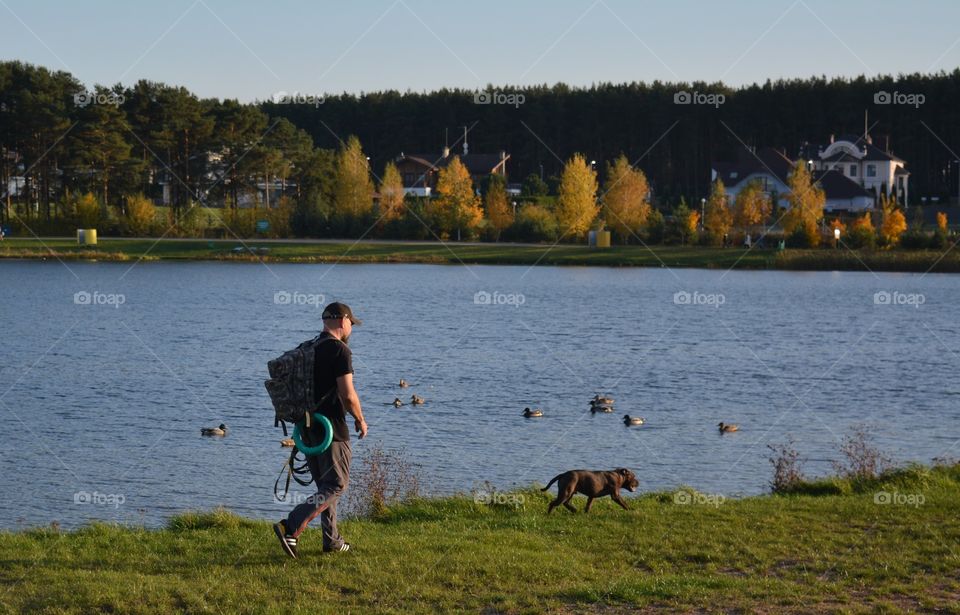 men walking with dog pet on a lake shore autumn landscape