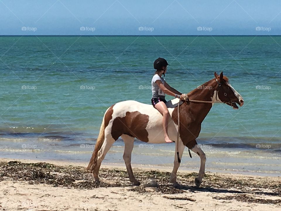 Barefoot girl horseback riding along seashore