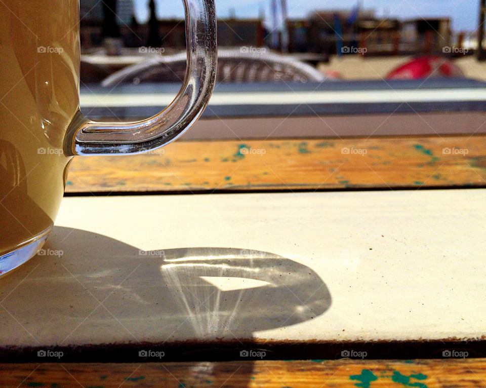 Handle of a cup of coffee reflects the sunlight on the table. 