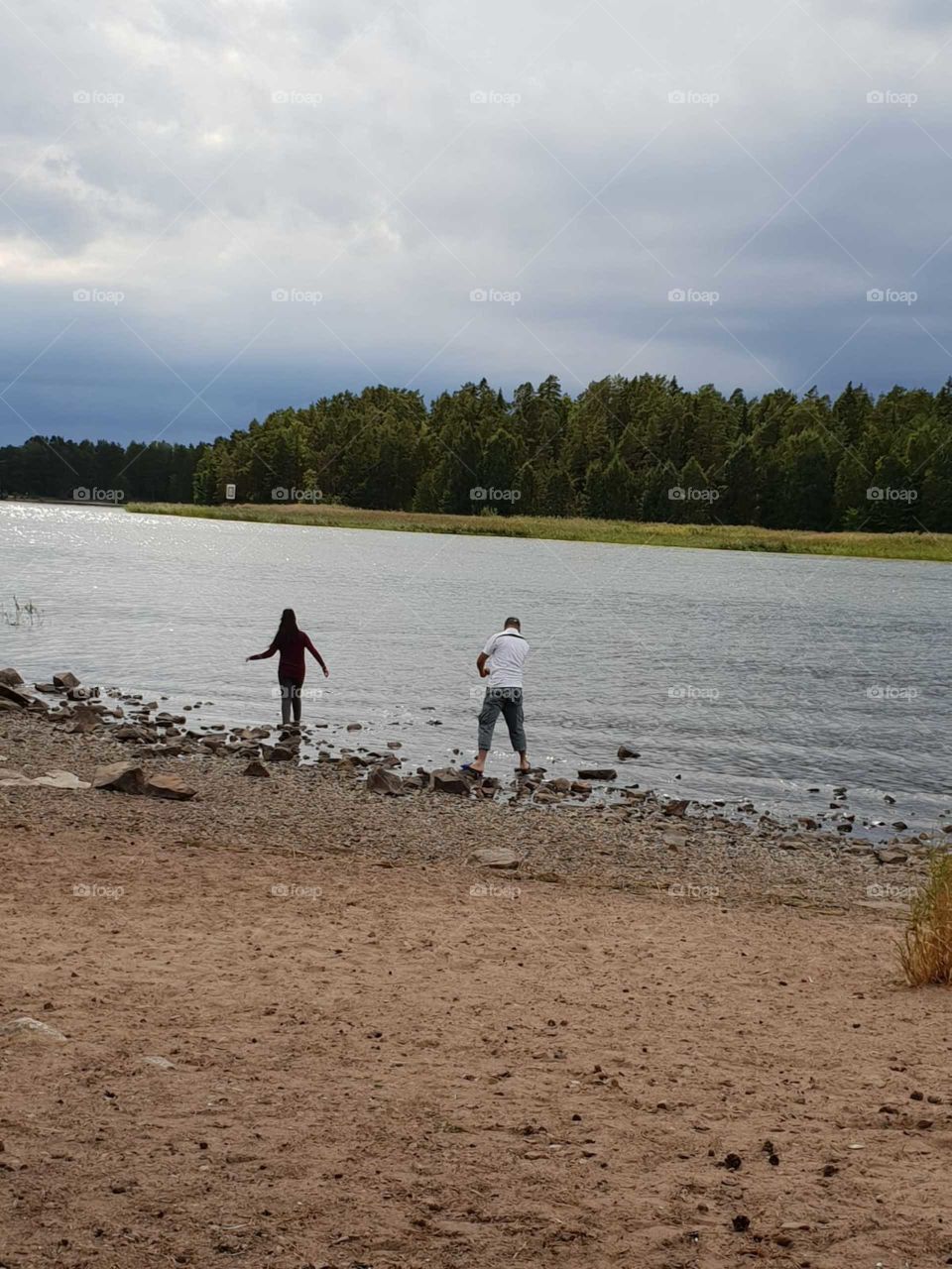 Two people throw stones at the lake.