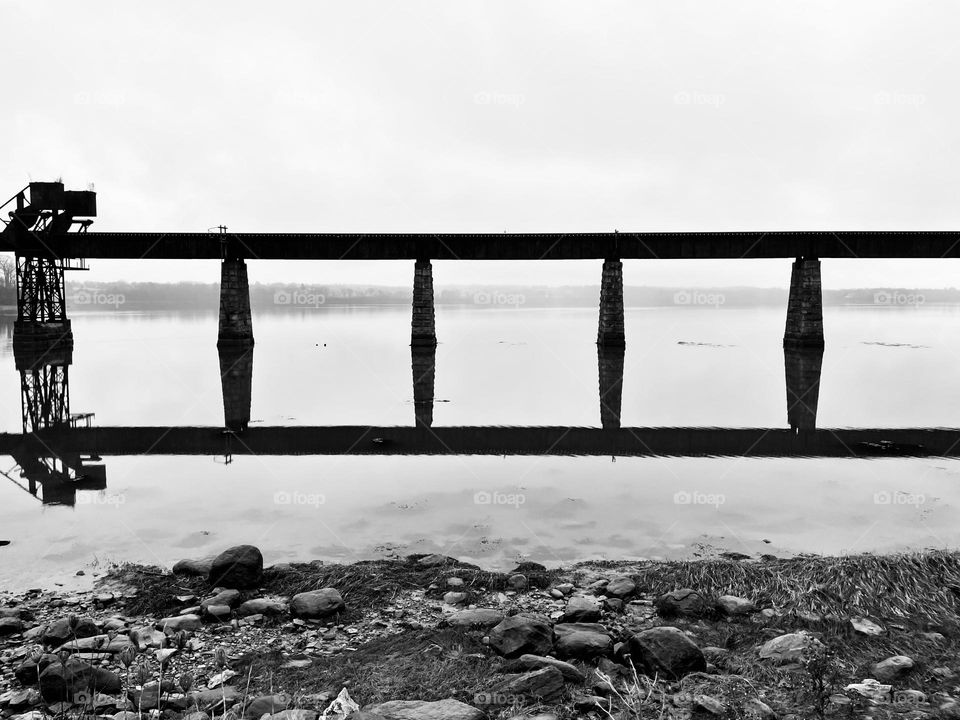 The reflection of a train trestle over a foggy river looks like a ladder across the horizon.