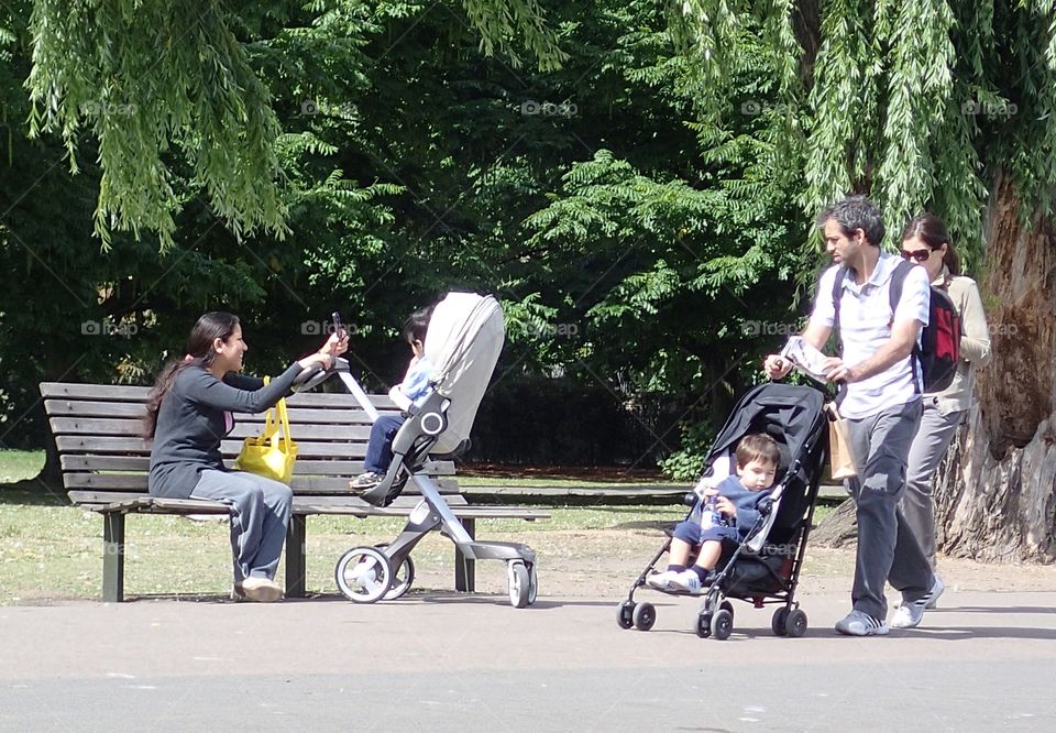 A woman with her son on a park bench and a couple with their son out for a stroll on a sunny summer day in Regents Park in London. 