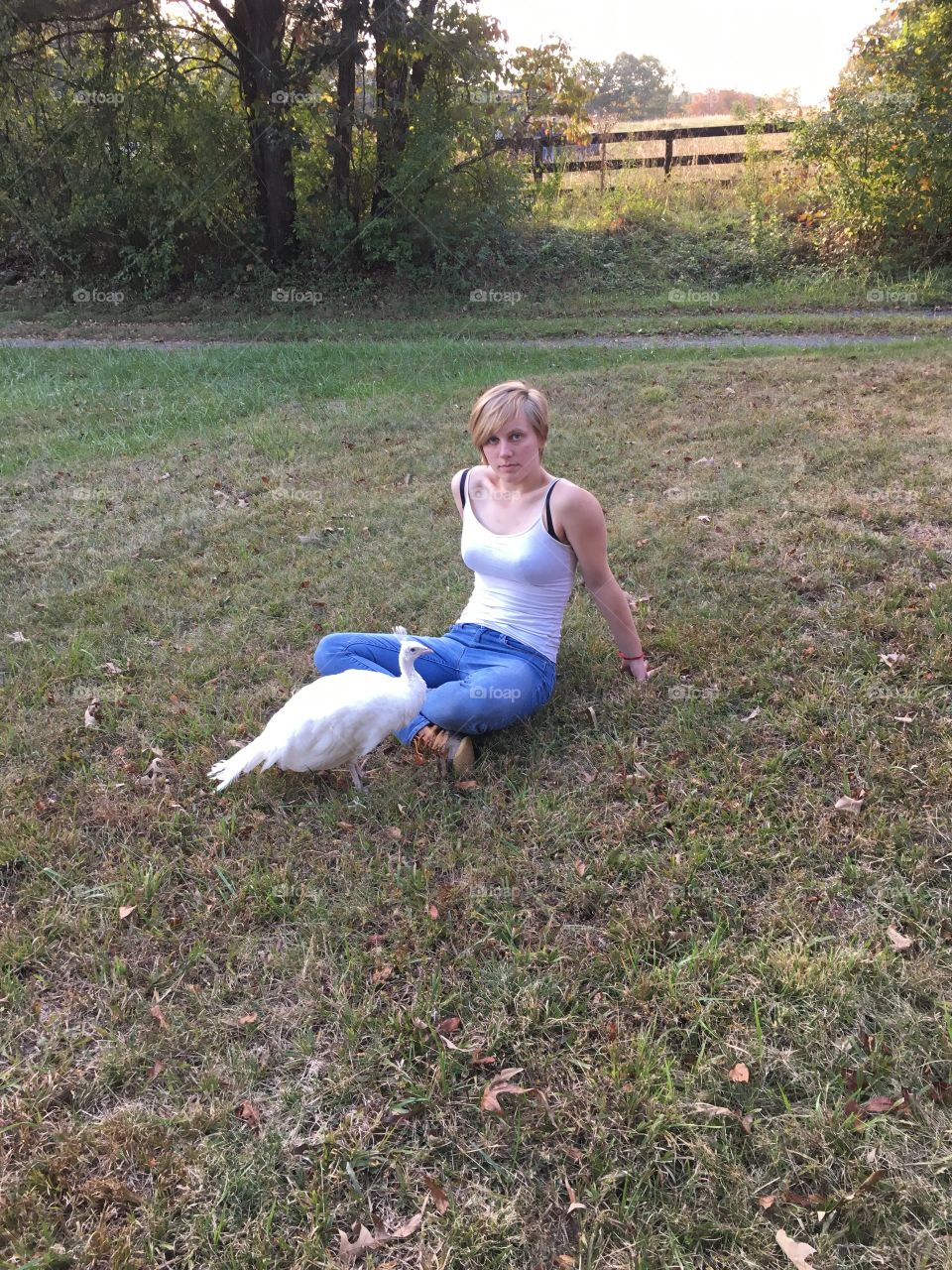 A beautiful young woman poses with her beautiful young leucistic peacock in her yard