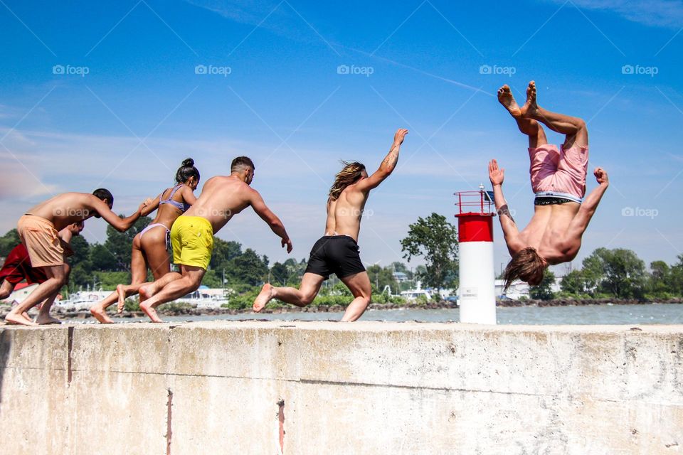 Group of young people is jumping from the pier to have a swim