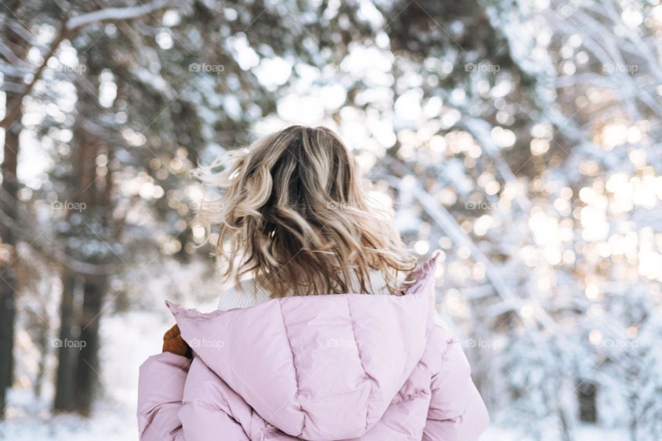 Blurred blonde woman in winter clothes in snowy winter forest, view from back