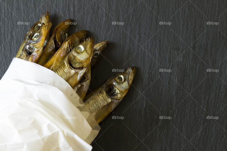 smoked fish. Fresh smoked little anchovies in a paper bag on the slate stone board . copy space for text