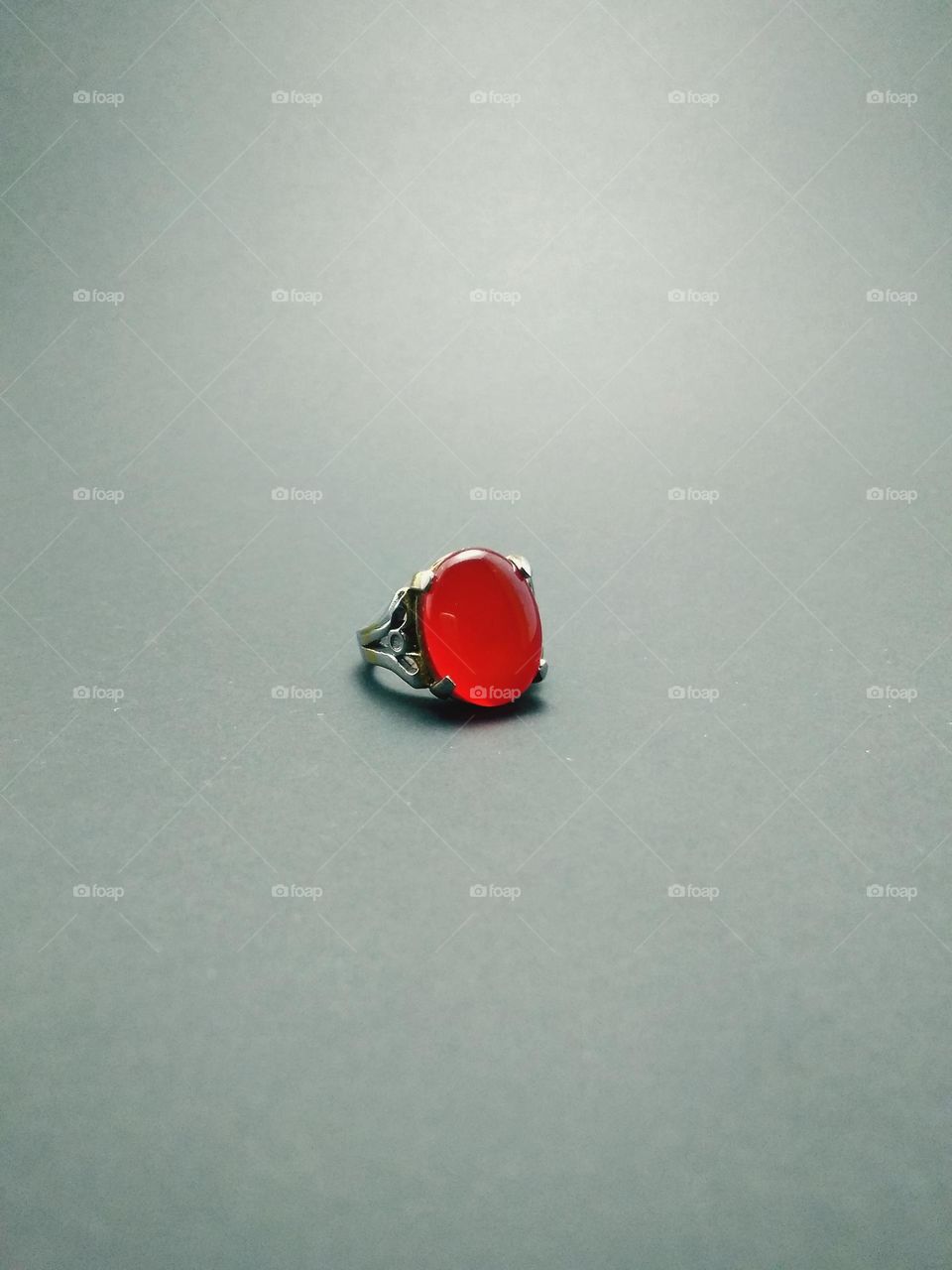 women's jewelry in the form of a ring with red chalcedony agate oval in shape, with a titanium ring photographed in the studio on a gray background.