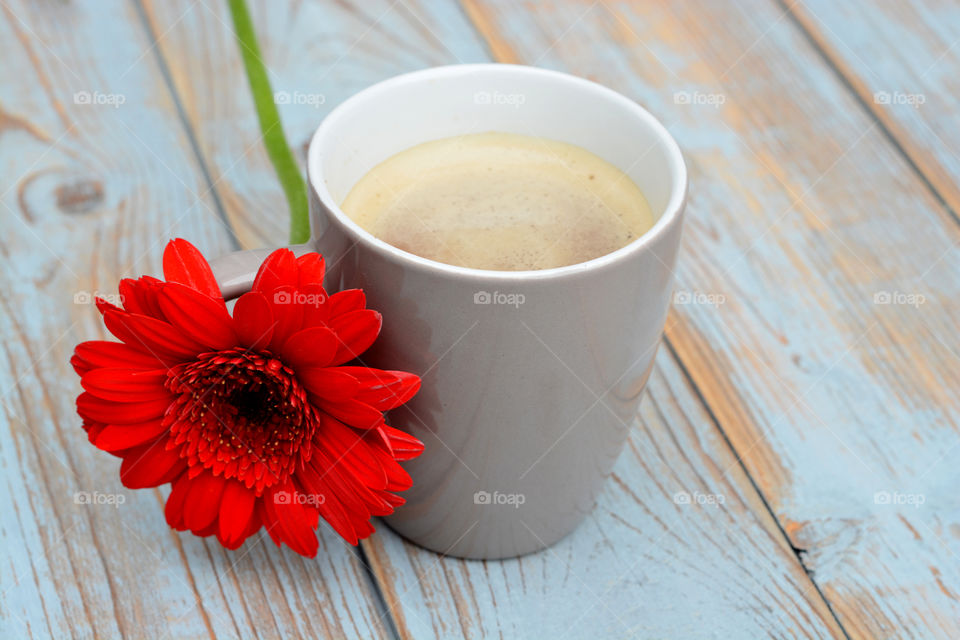 cup of coffee with red daisy flower on a wooden table background