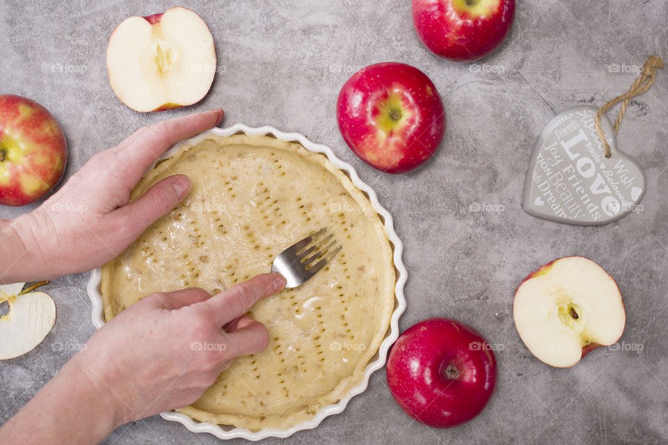 homemade baking, shortcrust pastry for apple pie in a baking dish, a woman's hand pierces the dough with a fork