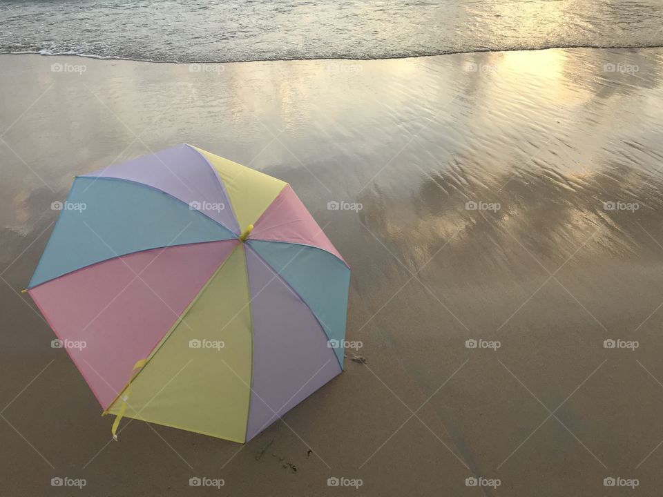 colorful pastel umbrella putting on clear beach with sea wave, cloud reflection and golden sun light