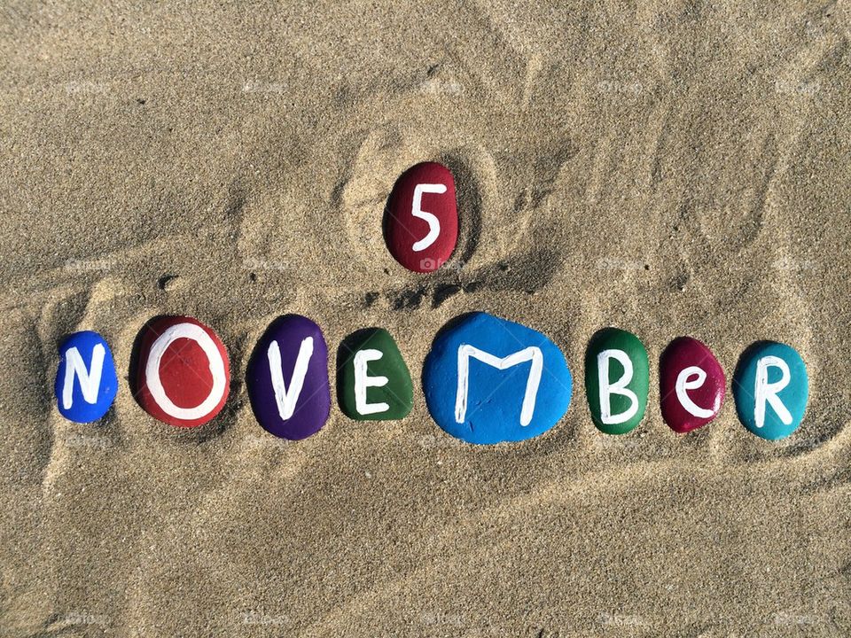 5 November day on colored stone letters with sand background