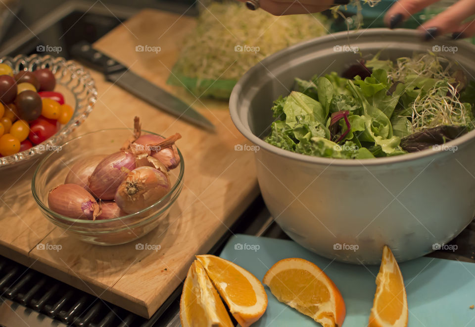 Hands preparing food with French cuisine essentials shallots, organic mesclun salad, tomatoes and knife on cutting board with fresh cut orange citrus for natural dressing