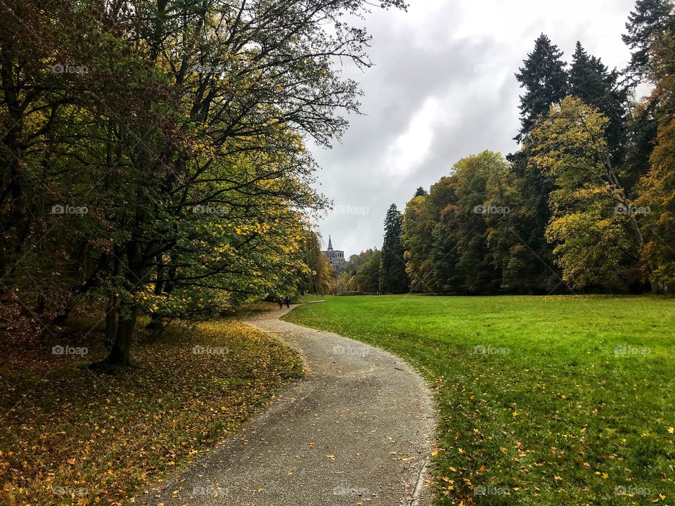 A small pathway next to the green grass, and surrounded by trees are changing colors , and the far side has a castle . The sky was cloudy gray and there was no sunlight , I walking that lane and enjoying the view