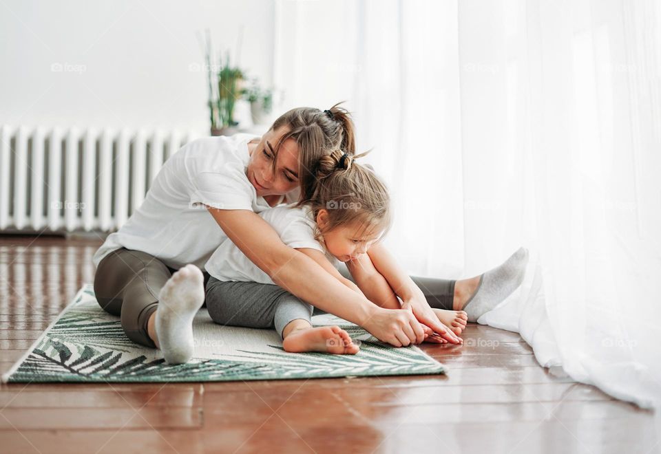 Happy mom and little daughter doing morning yoga together at bright interior home