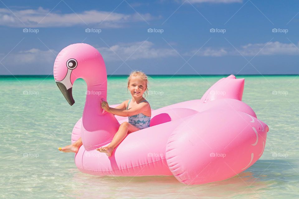 Barbie style. Adorable little Caucasian girl swimming on inflatable pink flamingo on sea