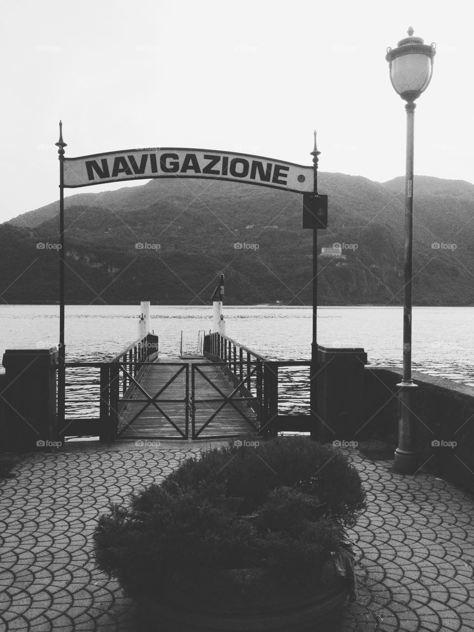 Black and white photo of an Italian pier with a sign saying ‘Navigazione’. There’s a small gate and a street light.