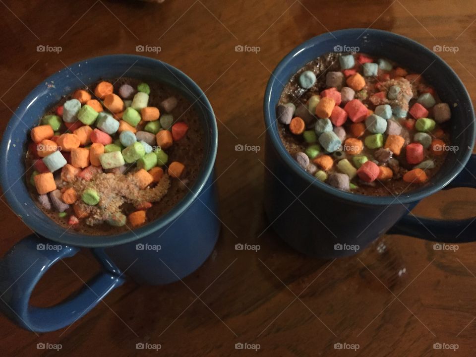 Two blue mugs of hot chocolate with many colored marshmallows on top. 