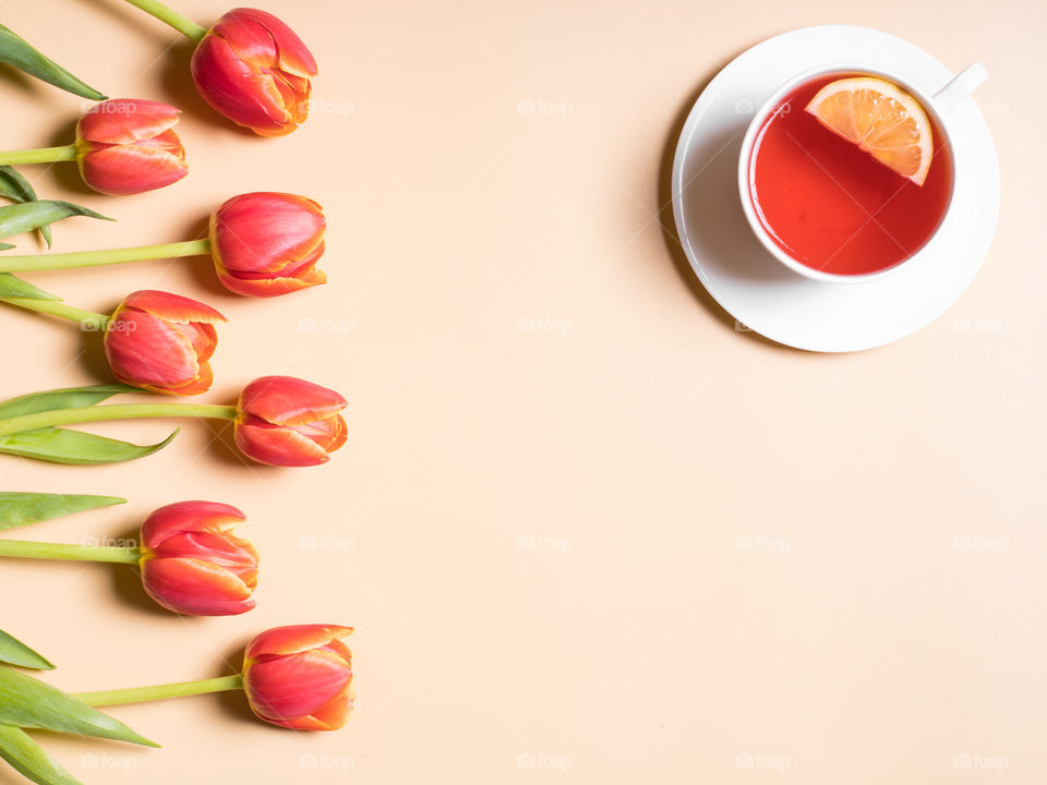 Colourful flat lay with red tulips and a cup of tea in a white cup with a slice of lemon. Copy space in the middle