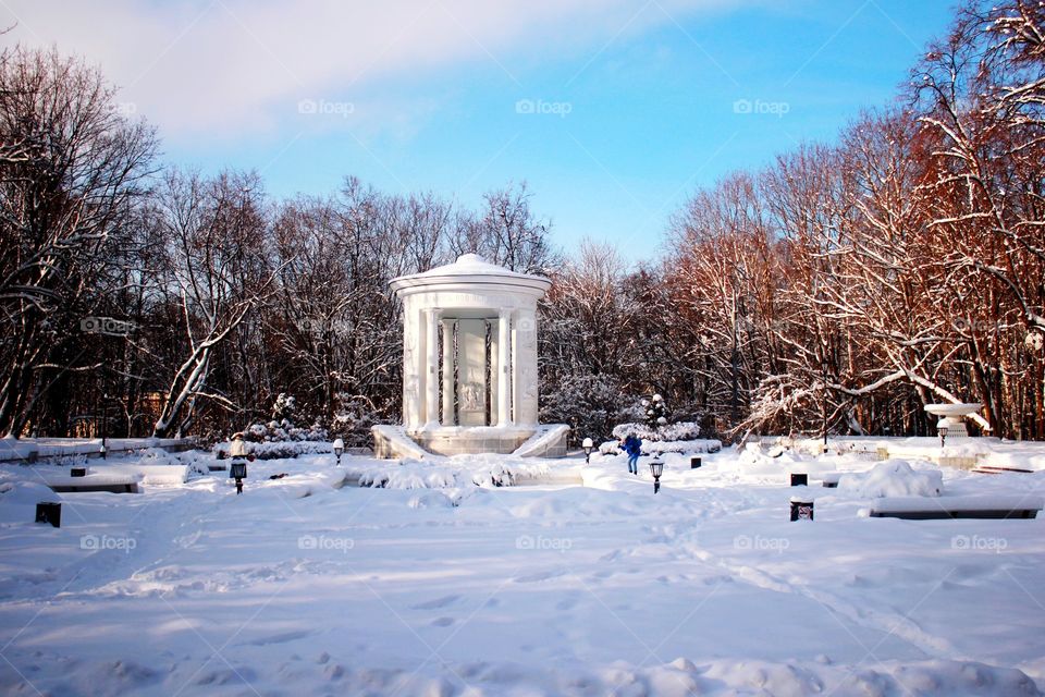 White gazebo in a park, snow-covered pavillion, trees and people, wonderful sunny winter day