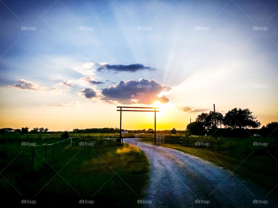 Sunset on the road home to a rural countryside farm with rays of light shooting from a cloud in the blue evening sky