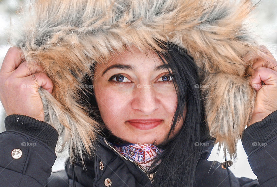Close up winter portrait of young and cute woman in black jacket with furry hood on her head.