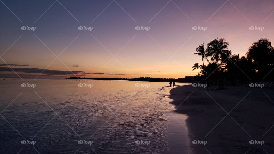 romantic beach sunset in Mexico. silhouettes and shadows of couple walking along Shoreline in the evening with palm trees